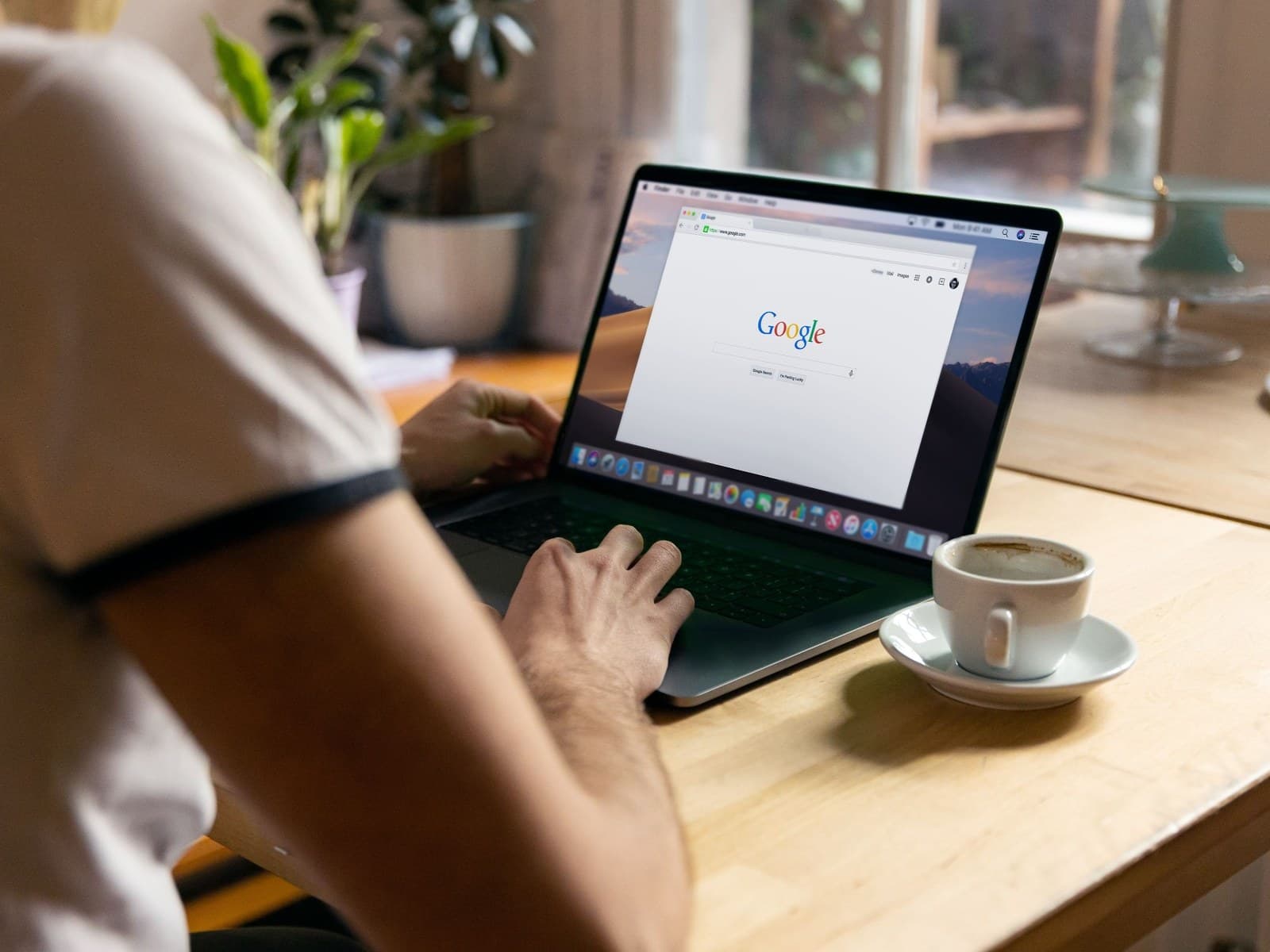 Iemand zoekt op Google op een laptop met een kop koffie ernaast